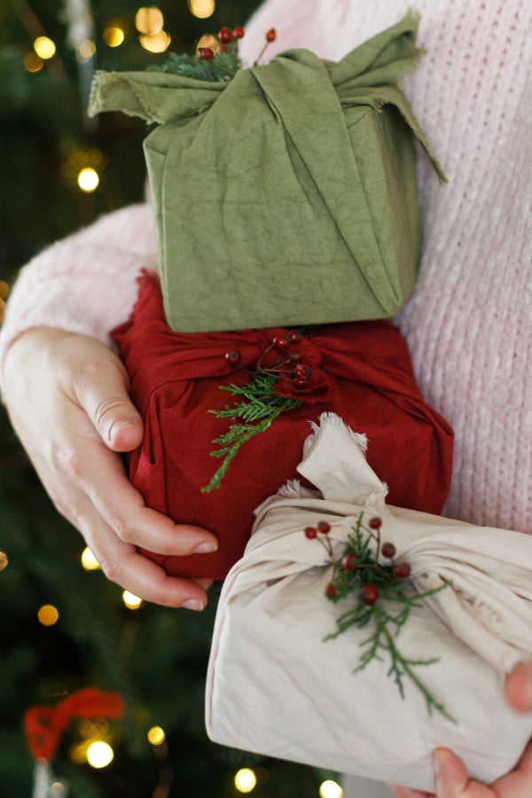 Someone holding x3 christmas presents wrapped in cloths.