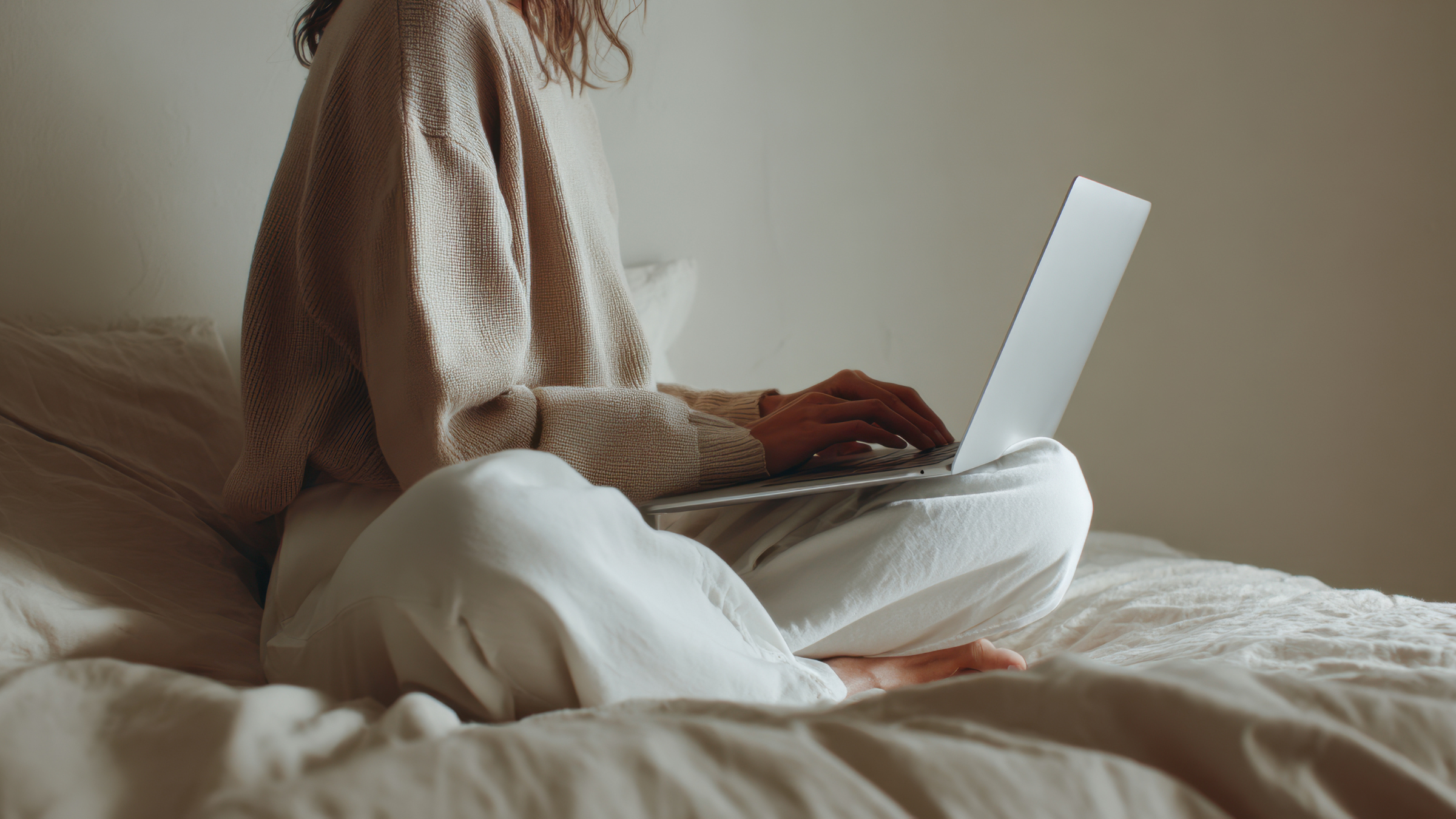Someone in neutrals sitting in a neutral room on their laptop.