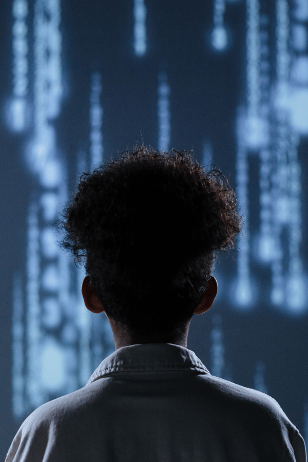 A young girl stands facing away from us, staring at a screen full of AI code. 