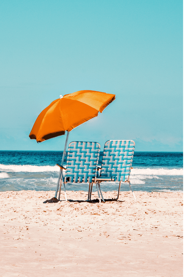 Two deck chairs look out to see with an orange umbrella above them. 