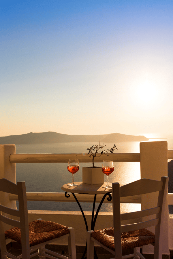 Two Aperol sprtiz glasses sit on a table on a veranda looking out to an Italian sunset. 