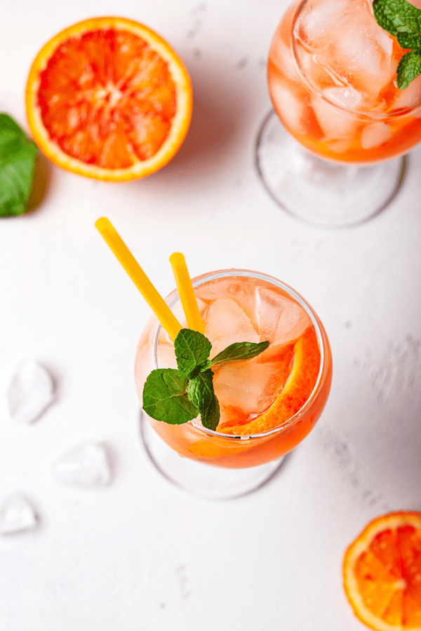 An aesthetically pleasing flatlay of a couple of glasses of Aperol spritz and oranges. 