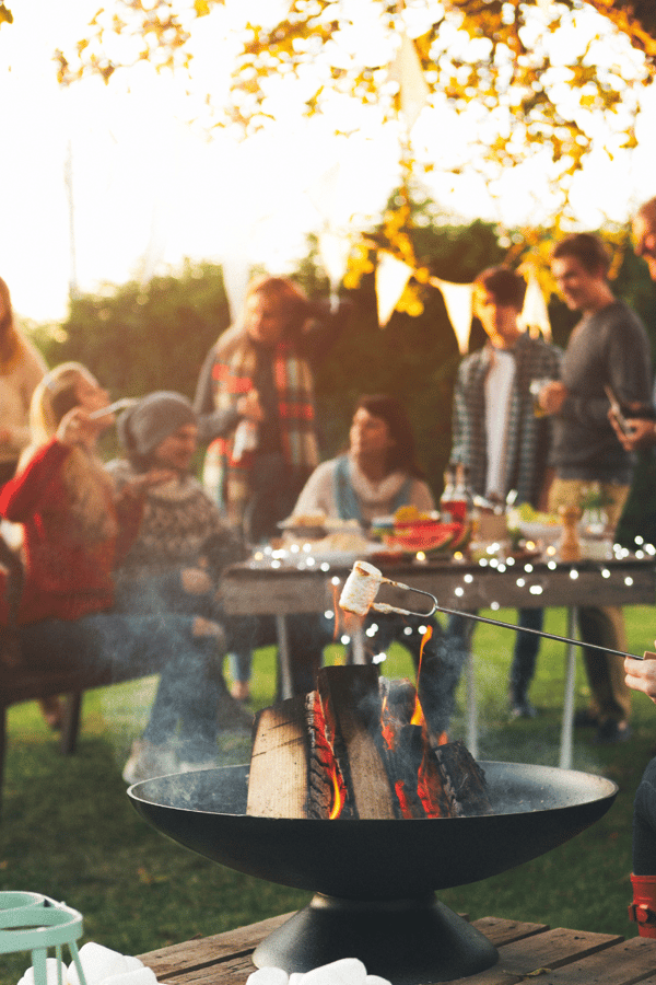 A group of people gathered around a BBQ enjoying eachother's company and having a lovely evening together thanks to the BBQ.