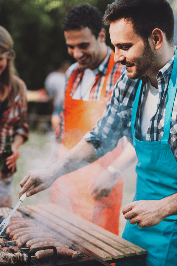Two men wearing aprons whilst they cook at a BBQ.