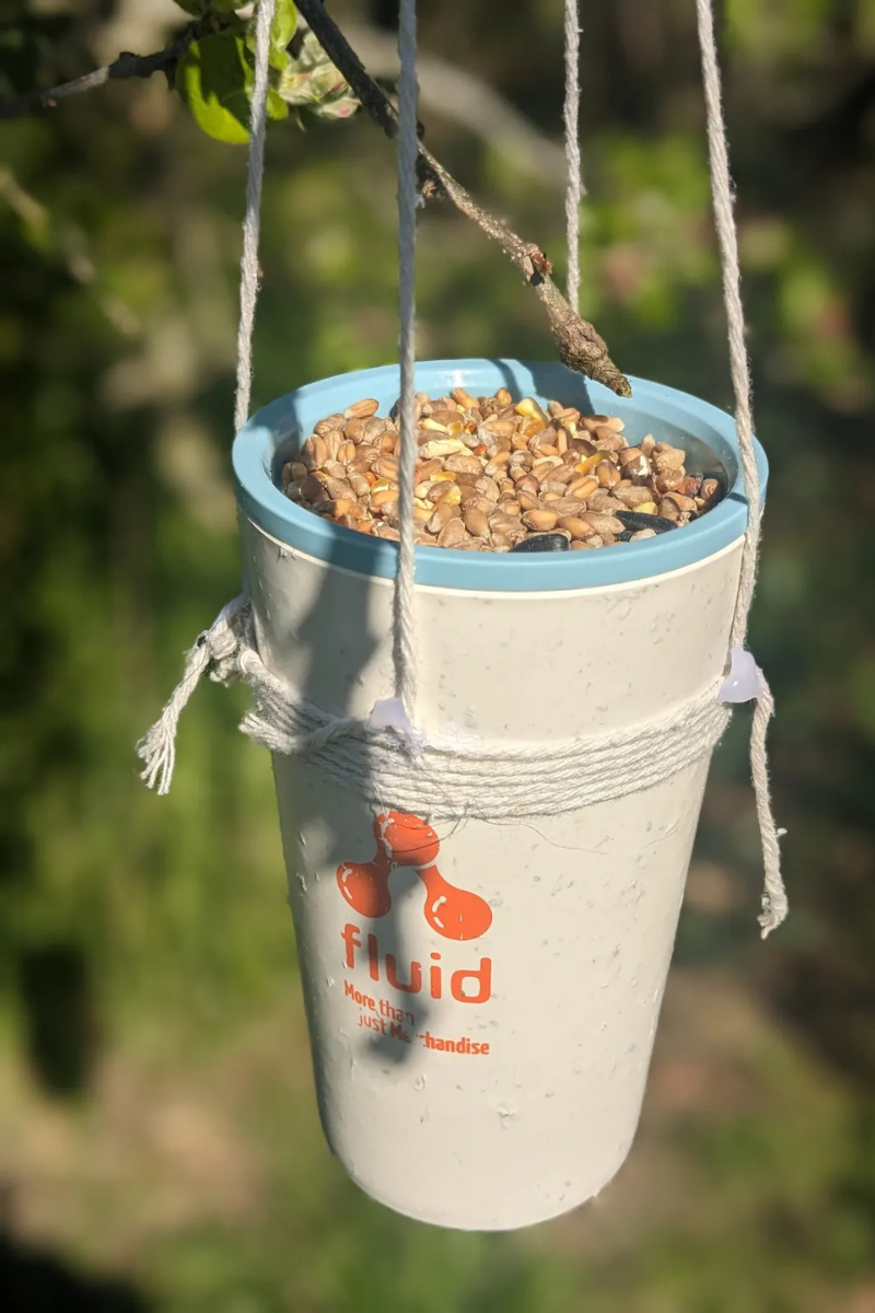 A photo of an old travel cup with 'Fluid' branded on it upcycled into a bird feeder. 