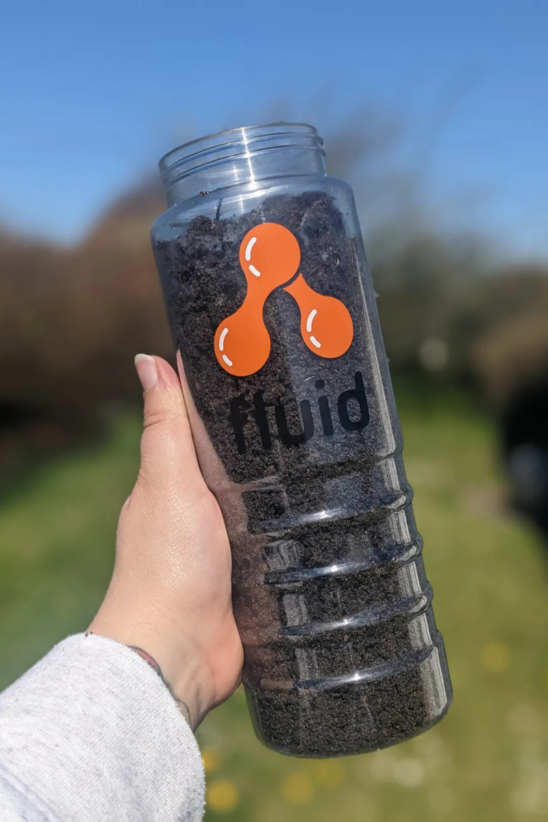 A photo of a plastic reusable branded bottle with 'Fluid' on the bottle filled with soil. 