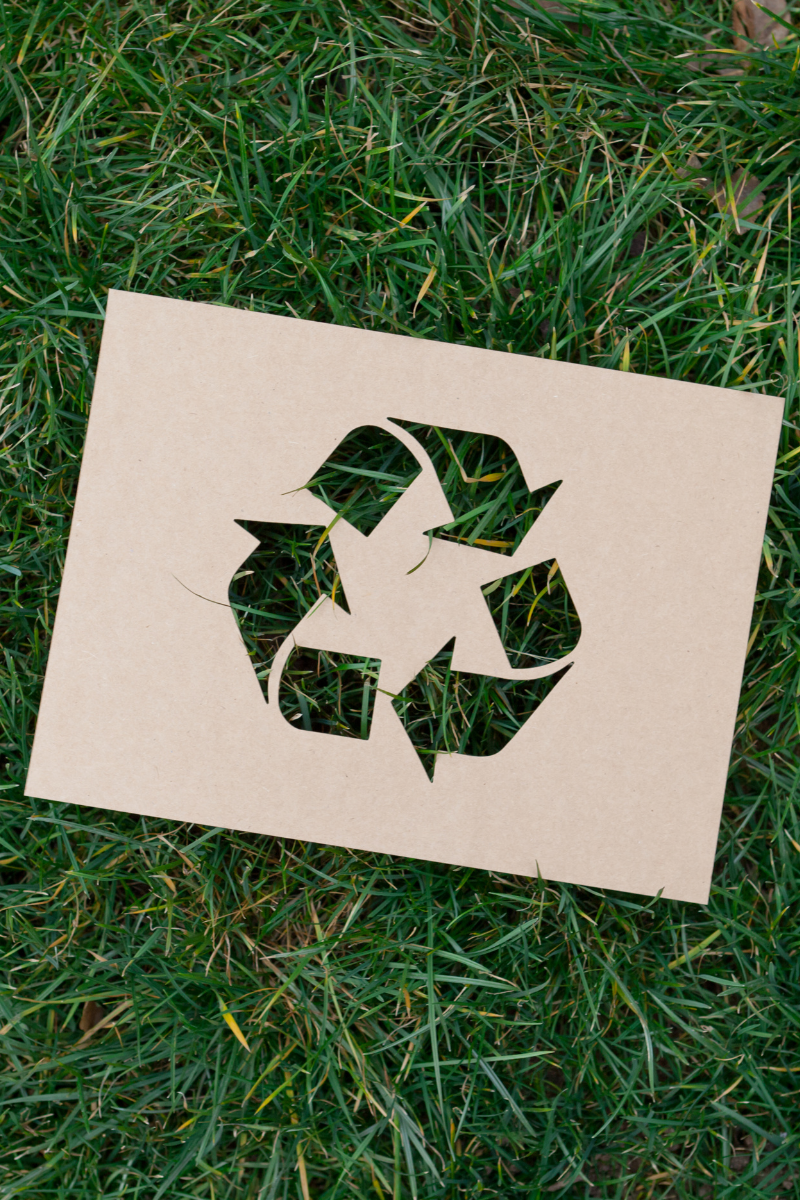 A photo of a cardbout cut-out recycle sign on some grass. 