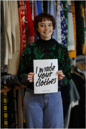 A woman who works at Notjust holding up a sign that says, "I made your clothes". 