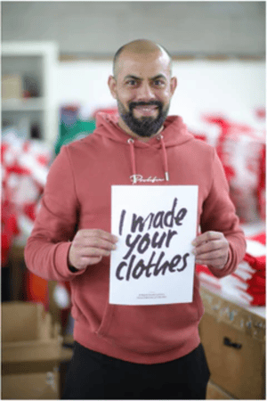 A man who works at Notjust holding up a sign that says, "I made your clothes". 