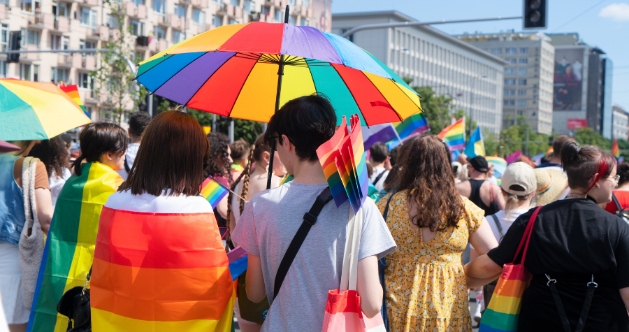 People using a rainbow umbrella during a Pride march.