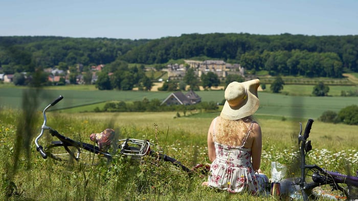 A girl sitting in a field in summer overlooking the countryside wearing a hat.