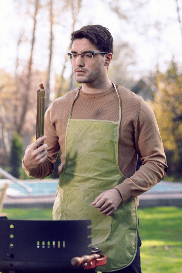 Typical Dad BBQ with a man wearing an apron, staring at some meat, working hard.