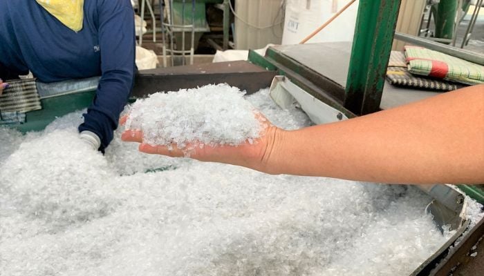Someone's hand holding lots of recycled plastic pellets over a massive bucket of more recycled plastic pellets. 