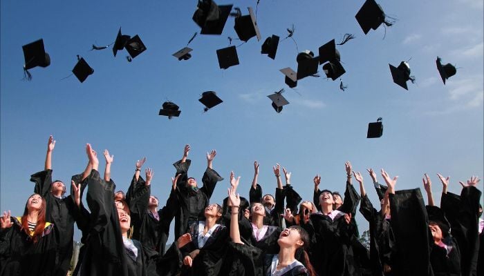 Recent university graduates celebrating by throwing their graduation caps into the air. 