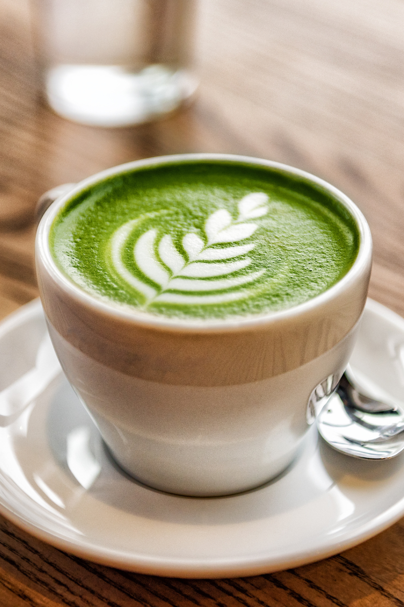 a mug full of bright green matcha latte with some matcha latte art on it.