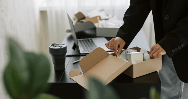 An office worker is excited to open a merch pack gift box at their desk.