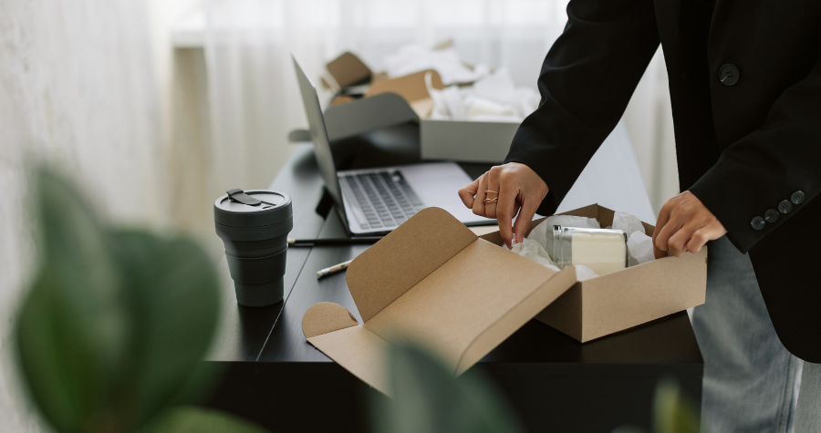 An office worker is excited to open a merch pack gift box at their desk.