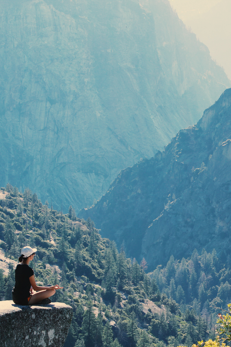 someone enjoying a wellness retreat in the mountains by meditating on a cliff edge. 