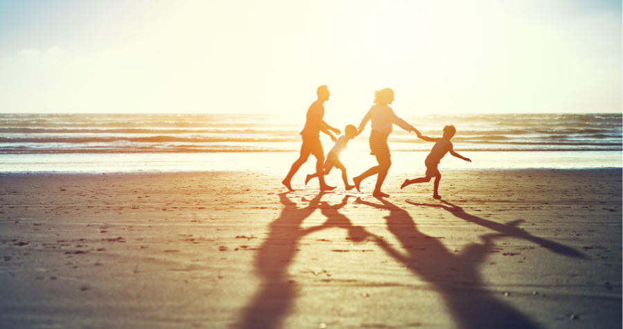 A family of four silhouetted against a sunset, running across a beach holding hands. 
