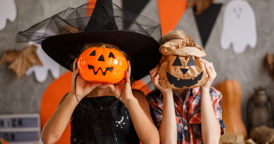 Two kids dressed up for Halloween holdiong up pumpkins in front of their faces.